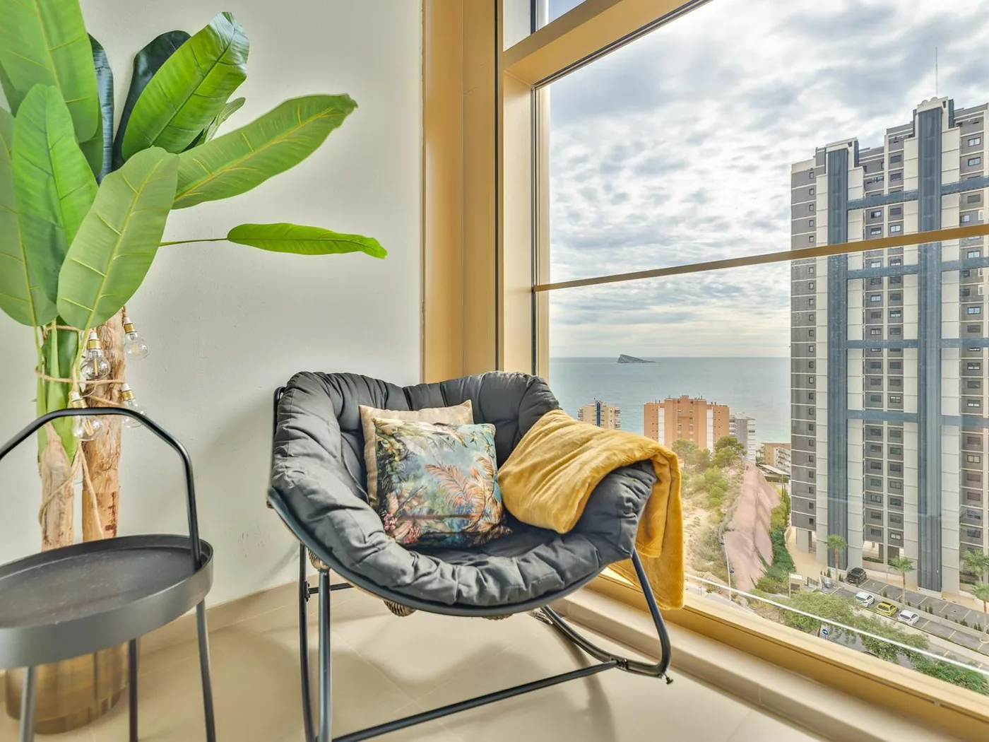Rincón de lectura junto al ventanal de suelo a techo en Gold & Gris, con Benidorm al fondo